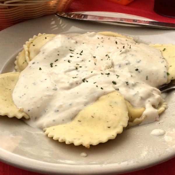 Ravioli pasta covered in creamy white sauce and sprinkled with herbs on a white plate.