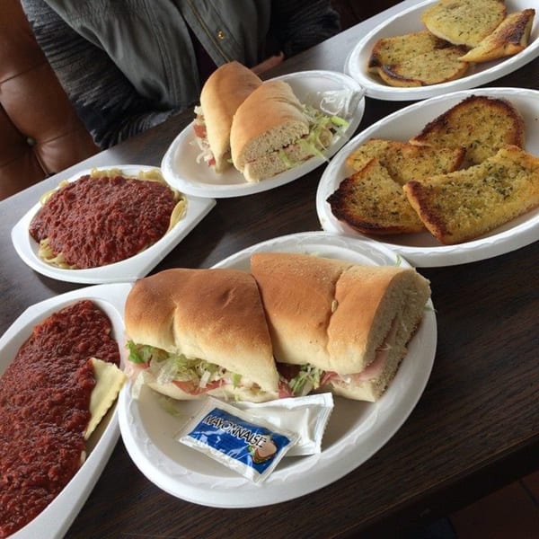 Italian grinders, spaghetti with red sauce, and garlic bread on white plates at The Grinders & Spaghetti House.
