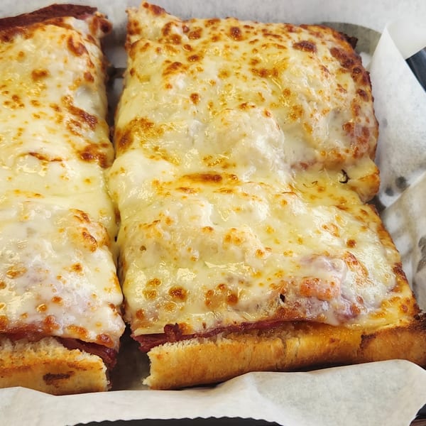 Two halves of a cheesy Italian grinder sandwich with melted, bubbly cheese on top.