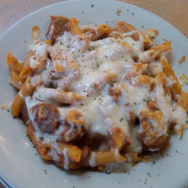 Baked penne pasta with meatballs, marinara sauce, and melted mozzarella cheese, garnished with herbs.