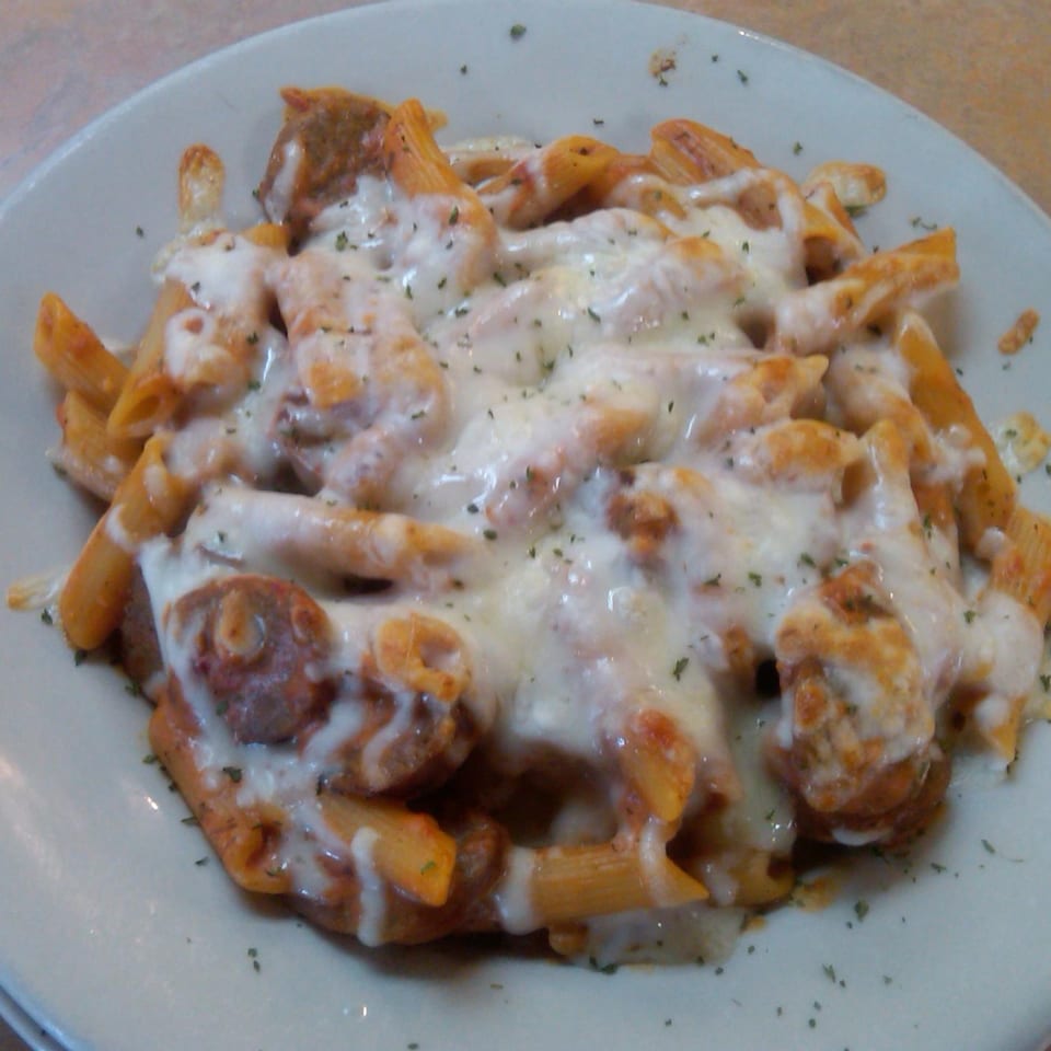 Baked penne pasta with meatballs, marinara sauce, and melted mozzarella cheese, garnished with herbs.