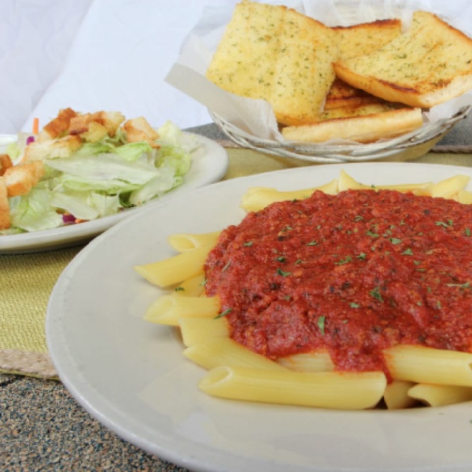 Penne pasta with red sauce, a side salad with croutons, and a basket of garlic bread.