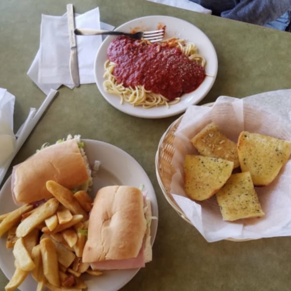 Spaghetti with red sauce, a grinder sandwich with fries, and garlic bread on a green table.