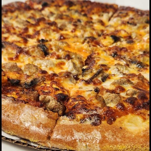 Close-up of a freshly baked Italian pizza from The Grinders & Spaghetti House, topped with sausage and mushrooms.