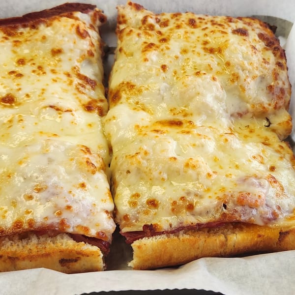 Two cheesy Italian grinders with melted, bubbly cheese and toasted bread, served in a paper-lined basket.