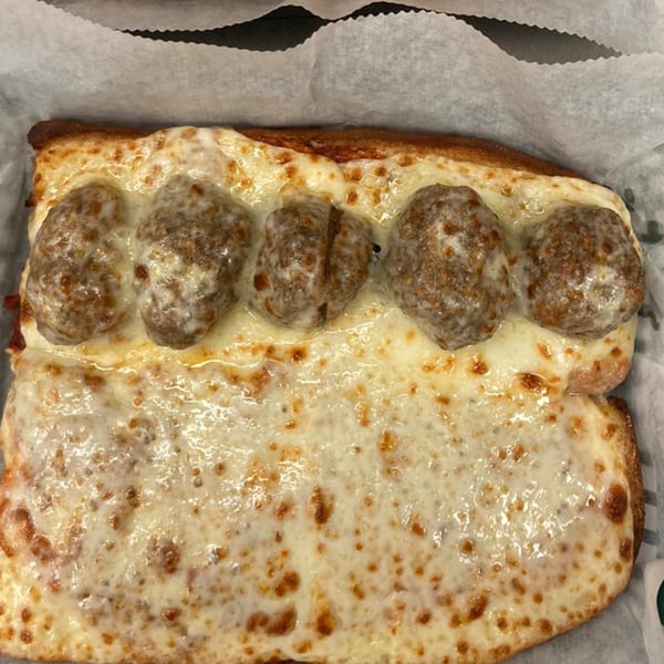 A meatball grinder from The Grinders & Spaghetti House, topped with melted cheese in a paper-lined basket.