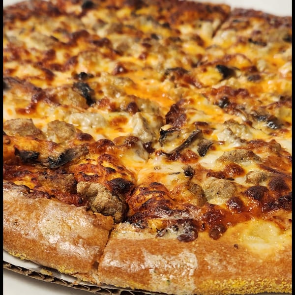 Close-up of a Grinders & Spaghetti House pizza with sausage, mushrooms, and melted cheese.